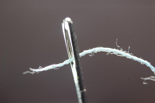 Macro photograph of sewing needle. Small needle with thread in the eyelet, isolated over the black background.
