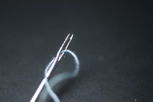 Macro photograph of sewing needle. Small needle with thread in the eyelet, isolated over the black background.