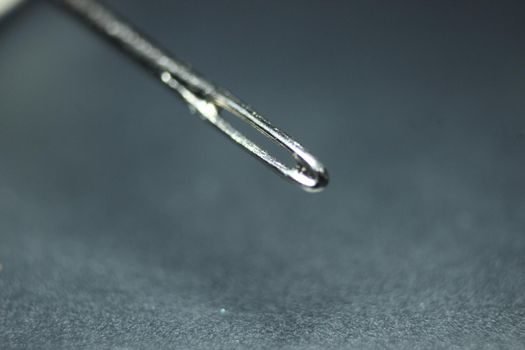 Macro photograph of sewing needle. Small needle with empty eyelet, isolated over the black background.