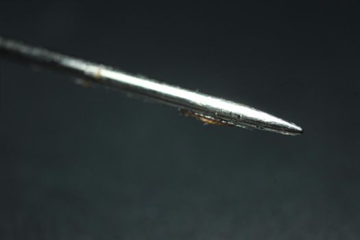 Macro photograph of sewing needle. Small needle isolated over the black background.