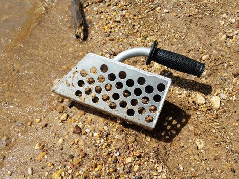 metal scooper on beach with sand and rocks and water