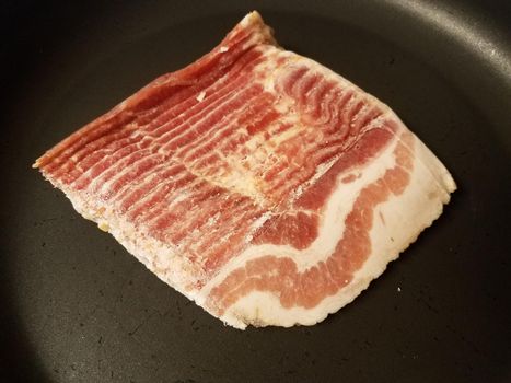 frozen bacon meat strips in frying pan or skillet