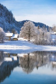 Idyllic winter landscape: Reflection lake, house and snowy trees and mountains