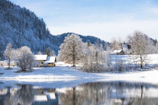 Idyllic winter landscape: Reflection lake, house and snowy trees and mountains