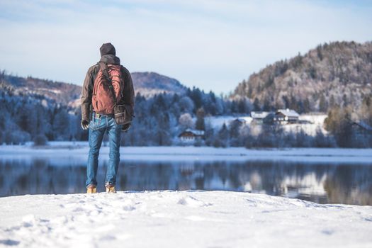 Sporty Caucasian man is at the lakeshore, enjoying the view. Winter landscape.