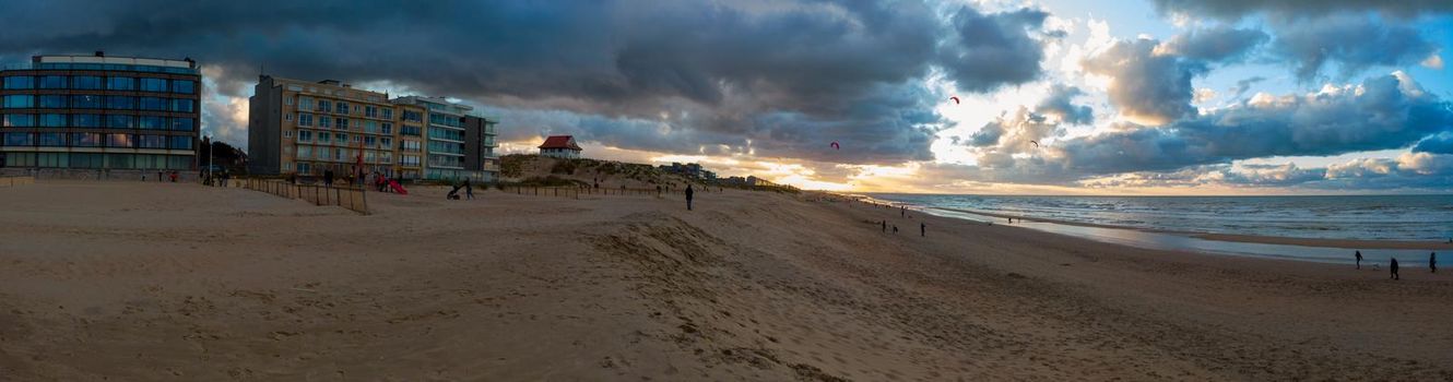 Panoramic view on the beach of Sint-Idesbald in Koksijde at De Panne at sunset with a glowing cloudy sky with some people on it