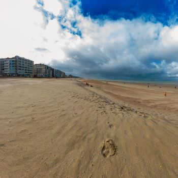 Empty beach with a footprint in Sint-Idesbald at Koksijde in autumn with a cloudy sky with some people in the background and the sea