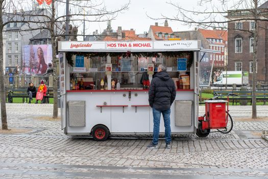 Copenhagen, Denmark - December 16, 2020: A man standing at a traditional hot dog cart in the city centre.