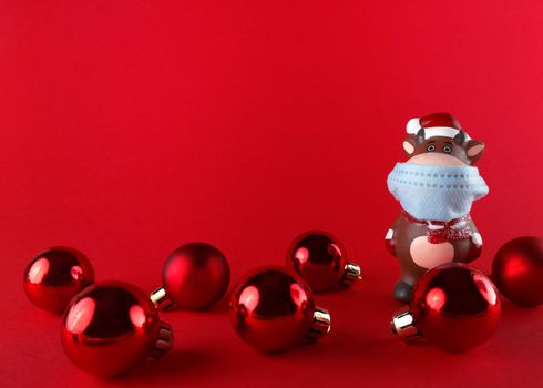 Ceramic statuette of Ox in medical mask and Christmas balls on a red background with copy space. Symbol of new year 2021.