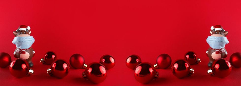 Ceramic statuettes of Ox in medical mask and Christmas balls on a red background. Wide banner with copy space. Symbol of new year 2021.