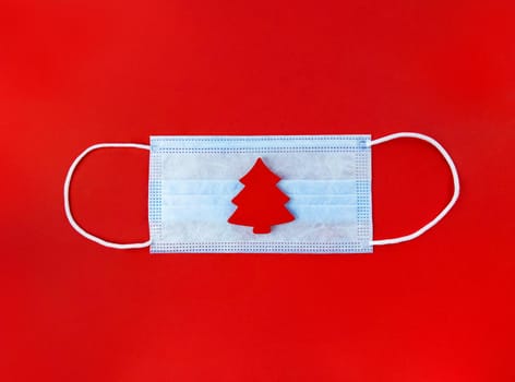 Medical mask and wooden christmas tree on a red background.