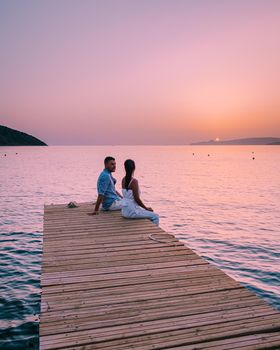 young romantic couple in love is sitting and hugging on wooden pier at the beach in sunrise time with golden sky. Vacation and travel concept. Romantic young couple dating at seaside. Crete Greece