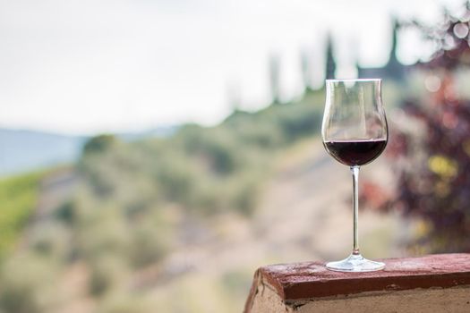 Enjoying a glass of red wine at Tuscany, Italy. Blurry wine yards in the background.