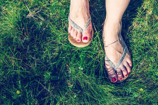 Closeup of flip flops or sandal on green grass, red nail polish