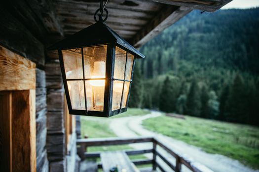 Rustic lantern is shining over the veranda, alpine hut