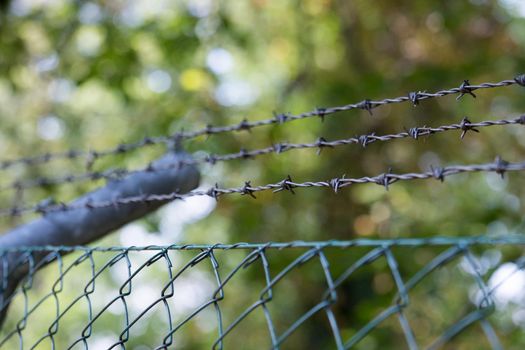 Barbed wire on a metal fence to demarcate the border, closeup, blurry background