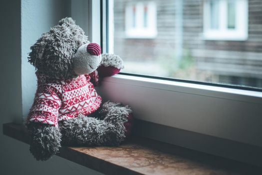 Cute teddy bear is sitting on the windowsill, looking out of the window