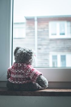 Cute teddy bear is sitting on the windowsill, looking out of the window