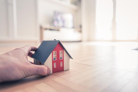 Adult hand is holding red house model, indoors. Concept for new home, property and estate