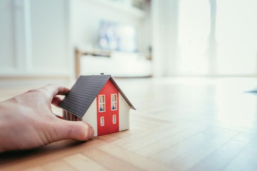 Adult hand is holding red house model, indoors. Concept for new home, property and estate