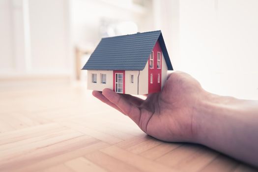 Adult hand is holding red house model, indoors. Concept for new home, property and estate