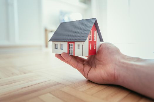 Adult hand is holding red house model, indoors. Concept for new home, property and estate