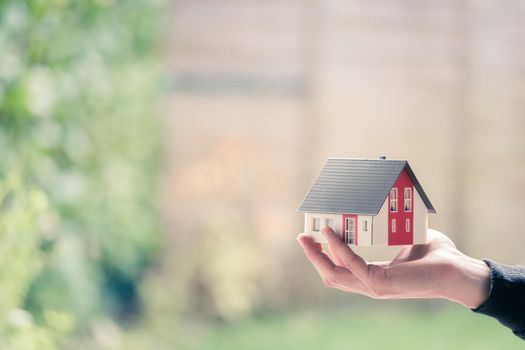 New home and house concept: Red house model outdoors in male hand, copy space