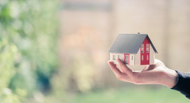 New home and house concept: Red house model outdoors in male hand, copy space