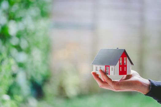 New home and house concept: Red house model outdoors in male hand, copy space