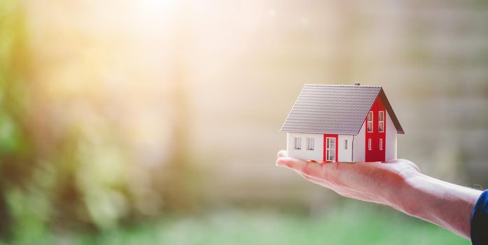 New home and house concept: Red house model outdoors in male hand, copy space