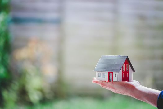 New home and house concept: Red house model outdoors in male hand, copy space