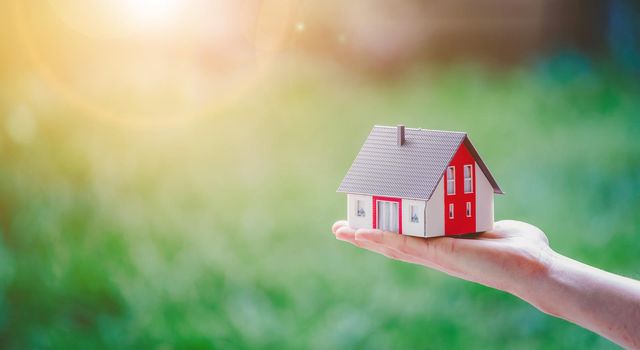 New home and house concept: Red house model outdoors in male hand, copy space