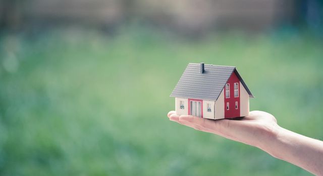 New home and house concept: Red house model outdoors in male hand, copy space