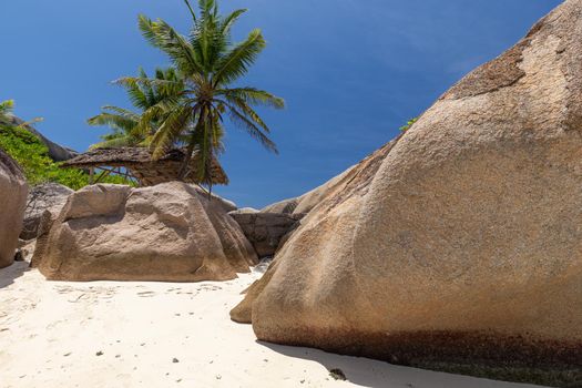 Beautiful beach Anse Source D'Argent on Seychelles island La Digue with white sand, granite rocks on the beach, palm trees, wooden cottage and blue sky 