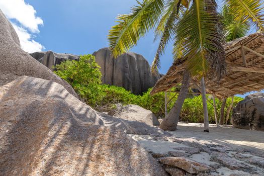 Beautiful beach Anse Source D'Argent on Seychelles island La Digue with white sand, granite rocks on the beach, palm trees, wooden cottage and blue sky 