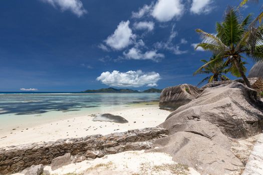 Beautiful beach Anse Source D'Argent on Seychelles island La Digue with white sand, granite rocks on the beach, palm trees, wooden cottage and blue sky 