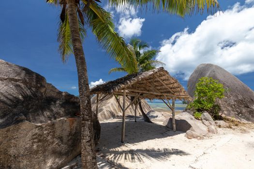 Beautiful beach Anse Source D'Argent on Seychelles island La Digue with white sand, granite rocks on the beach, palm trees, wooden cottage and blue sky 