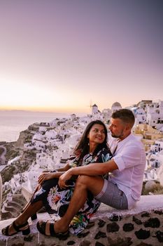 Santorini Greece, young couple on luxury vacation at the Island of Santorini watching sunrise by the blue dome church and whitewashed village of Oia Santorini Greece during sunrise during summer vacation, men and woman on holiday in Greece