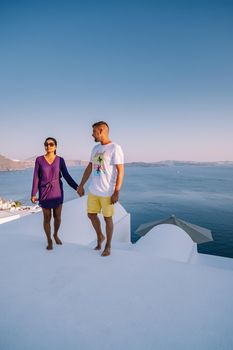 Santorini Greece, young couple on luxury vacation at the Island of Santorini watching sunrise by the blue dome church and whitewashed village of Oia Santorini Greece during sunrise during summer vacation, men and woman on holiday in Greece