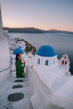 Santorini Greece, young couple on luxury vacation at the Island of Santorini watching sunrise by the blue dome church and whitewashed village of Oia Santorini Greece during sunrise during summer vacation, men and woman on holiday in Greece