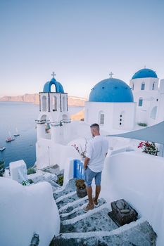 Sunset at the Island Of Santorini Greece, beautiful whitewashed village Oia with church and windmill during sunset, streets of Oia Santorini during summer vacation at the Greek Island, young men on luxury vacation Santorini