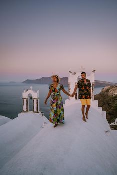 Santorini Greece, young couple on luxury vacation at the Island of Santorini watching sunrise by the blue dome church and whitewashed village of Oia Santorini Greece during sunrise during summer vacation, men and woman on holiday in Greece