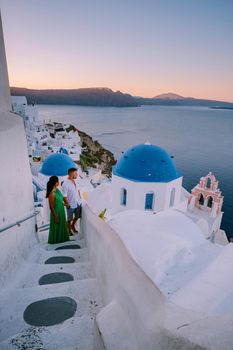 Santorini Greece, young couple on luxury vacation at the Island of Santorini watching sunrise by the blue dome church and whitewashed village of Oia Santorini Greece during sunrise during summer vacation, men and woman on holiday in Greece