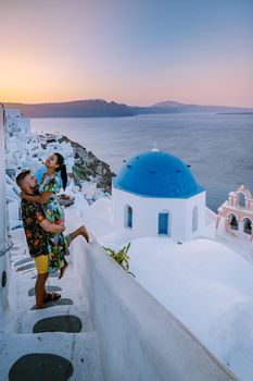 Santorini Greece, young couple on luxury vacation at the Island of Santorini watching sunrise by the blue dome church and whitewashed village of Oia Santorini Greece during sunrise during summer vacation, men and woman on holiday in Greece