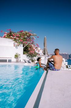 Santorini Greece, young couple on luxury vacation at the Island of Santorini watching sunrise by the blue dome church and whitewashed village of Oia Santorini Greece during sunrise during summer vacation, men and woman on holiday in Greece