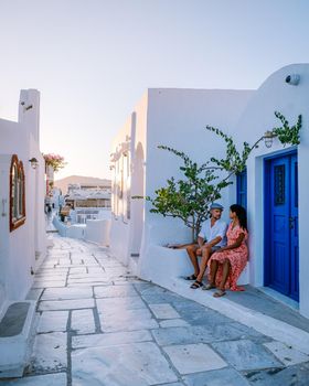 Santorini Greece, young couple on luxury vacation at the Island of Santorini watching sunrise by the blue dome church and whitewashed village of Oia Santorini Greece during sunrise during summer vacation, men and woman on holiday in Greece