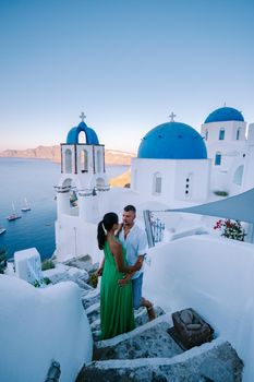 Santorini Greece, young couple on luxury vacation at the Island of Santorini watching sunrise by the blue dome church and whitewashed village of Oia Santorini Greece during sunrise during summer vacation, men and woman on holiday in Greece