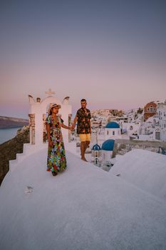 Santorini Greece, young couple on luxury vacation at the Island of Santorini watching sunrise by the blue dome church and whitewashed village of Oia Santorini Greece during sunrise during summer vacation, men and woman on holiday in Greece