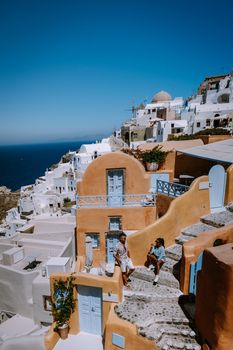 Santorini Greece, young couple on luxury vacation at the Island of Santorini watching sunrise by the blue dome church and whitewashed village of Oia Santorini Greece during sunrise during summer vacation, men and woman on holiday in Greece