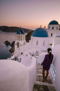 Sunset at the Island Of Santorini Greece, beautiful whitewashed village Oia with church and windmill during sunset, streets of Oia Santorini during summer vacation at the Greek Island Woman on luxury vacation Greece